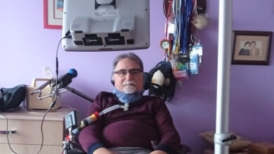 Dr Alper Kaya ALS-MNH Derneği Başkanı'trakeostomi açık şekilde önünde mikrofon başında fotoğraf çekiliyor.
