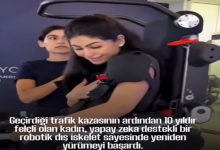 Bir kadın, yapay zekâ destekli robotik bir dış iskelet yardımıyla ayakta duruyor. Yanında ona destek olan bir görevli bulunuyor. Kadın gülümseyerek duygusal bir an yaşıyor. Alt kısımda, kazadan sonra 10 yıl boyunca felçli kaldığı ve bu teknolojiyle yeniden yürümeyi başardığı yazılı.