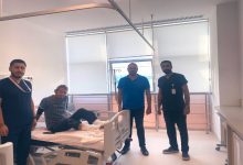 Aydınlık bir hastane odasında dört kişi görülüyor. Ortada, hastane yatağında oturan bir hasta var; ayakları bandajlı. Yanında üç sağlık çalışanı ya da görevli ayakta duruyor. Odanın büyük pencerelerinden gün ışığı süzülüyor, ortam temiz ve sakin bir tedavi alanı hissi veriyor.