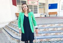 Nusret Şenay Anaokulu binası önünde, yeşil ceketli ve koltuk değnekleriyle ayakta duran öğretmen Hilal Demir’in fotoğrafı.