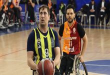 Bir spor salonunda tekerlekli sandalyede basketbol oynayan iki sporcu görülüyor. Önde topu elinde tutan sporcu şuta hazırlanırken, arkasındaki rakip oyuncu savunmada; maçın ciddiyeti ve rekabet duygusu öne çıkıyor.