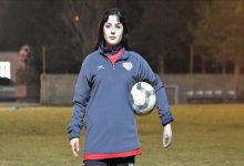 Hümeyra Alantaş, spor kıyafetiyle futbol sahasında ayakta dururken, sol protez kolunun altında topu tutarak poz veriyor.