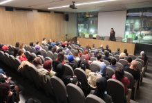 Yazar Espina Hande Ayas, kürsüde ayakta durarak konuşma yapıyor, katılımcılar salon koltuklarında oturarak konuşmayı dinliyor.