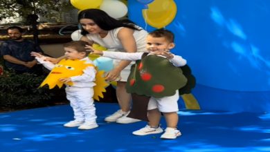 Mavi zeminli bir sahnede, kostüm giymiş iki küçük çocuk ve yanlarında onları yönlendiren bir kadın görülüyor. Çocuklardan biri güneş, diğeri ise ağaç temalı kostüm taşırken, etkinlik alanı sarı-beyaz-mavi balonlarla süslenmiş. Çocuklar sahnede neşeli bir şekilde izleyicilere doğru poz veriyor.