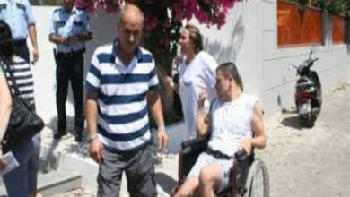 Tekerlekli sandalye kullanan engelli birey ve ailesi bir binanın önünde ayakta duruyor.