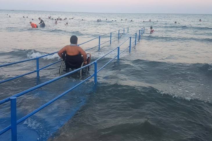 Tekerlekli sandalyeyle rampa kullanarak denizde bulunan erkek turist.