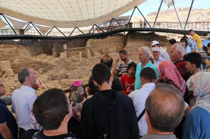 Göbeklitepe'de bulunan kafile, teraslı gezinti alanında rehber eşliğinde kalıntıları inceliyor.