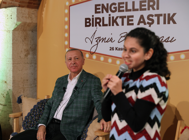 Cumhurbaşkanı Erdoğan otururken, elinde tuttuğu mikrofonla konuşan görme engelli genç kızı dinliyor.