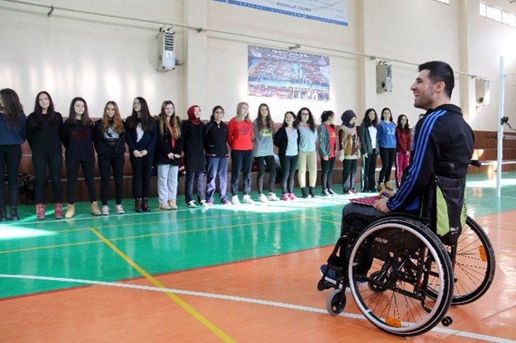 İlgili beden eğitimi öğretmeni, karşısında sıralanan öğrencilerine tekerlekli sandalyesinde ders veriyor.