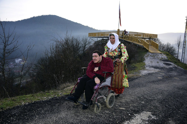 Anne Feride Kazan oğlunun oturduğu tekerlekli sandalyeyi asfalt yolda sürüyor.