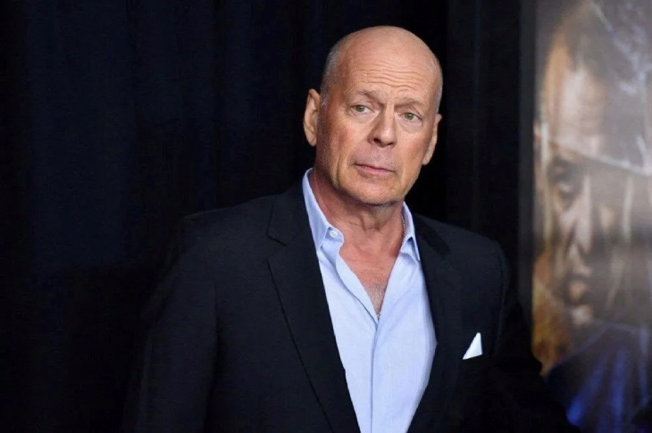 Bruce Willis üst düğmeleri açık mavi gömlek ve ceket kıyafetiyle objektife yansıyor.