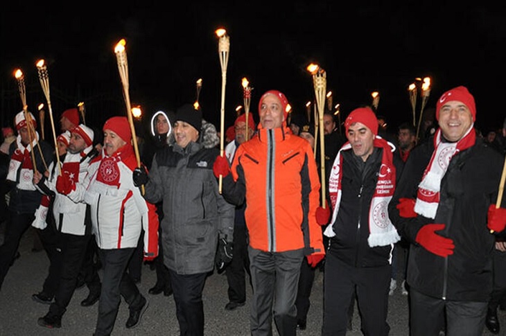 Akşam karanlığında elindeki meşalelerle bir arada yürüyüş yapan çok sayıda katılımcı objektife yansıyor.