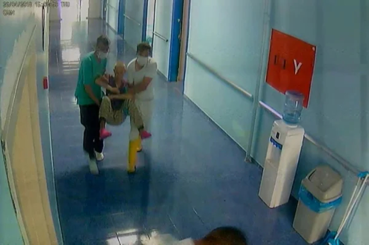 İki bakım merkezi personeli erkek zihinsel engelli Selim Serdaroğlu'nu kol ve bacaklarından tutarak taşıyor.