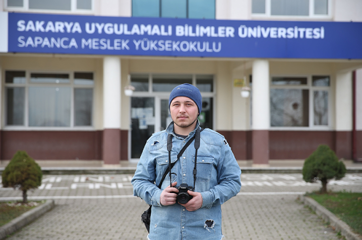 Görme engelli fotoğrafçı Emirhan Gümüş üniversite önünde fotoğraf makinesi tutarak poz veriyor.
