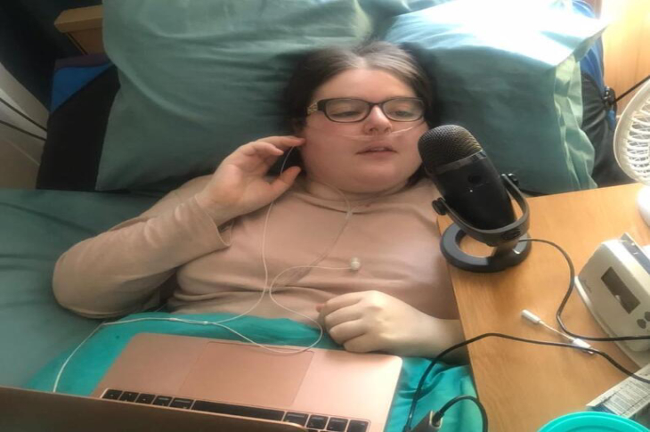 Yatağında uzanan burnuna oksijen yolu kablosu takılı Kara Jane Spencer bilgisayar kullanıyor ve stüdyo mikrofonu kullanıyor.