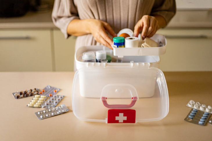 Kızıl haç logolu ilk yardım çantasını düzenleyen kadın ve masa üzerinde bulunan ilaç hapları.