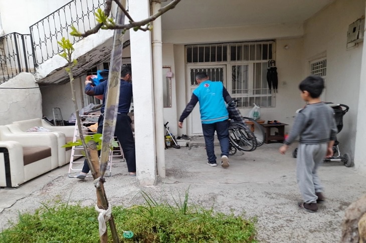 İhtiyaç sahibinin adresine tekerlekli sandalyeyi götüren iki görevli objektife yansıyor.