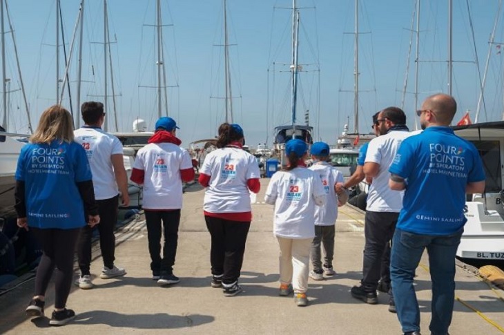 Yat limanında, takım halinde yelkenliye doğru ilerleyen özel gereksinimli çocuklar objektife yansıyor.