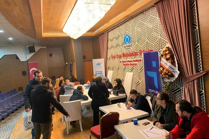 Aynı masada, yetkililerle birebir görüşen çok sayıda engelli birey objektife yansıyor.