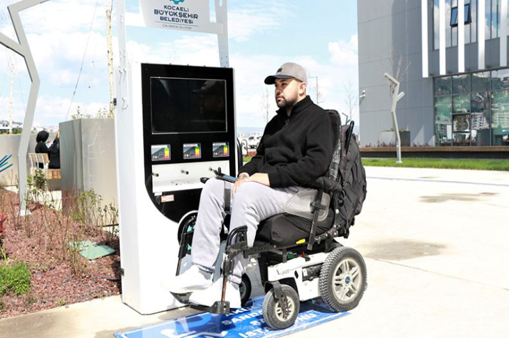 İstasyon önünde akülü sandalyesini şarj eden bedensel engelli erkek.