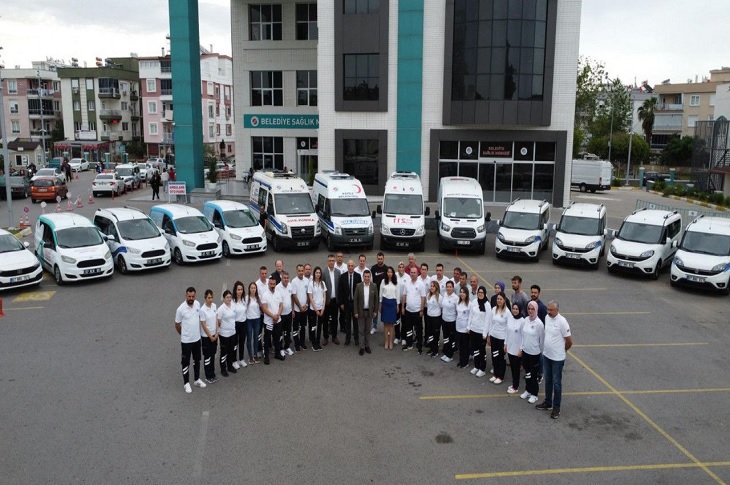 Belediye hizmet binası önünde hizmet aracı ve ambulanslarla poz veren çok sayıda sağlık görevlisi objektife yansıyor.