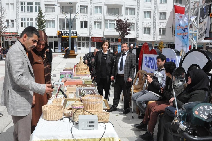 Açık hava, masa üzerinde sergilenen ürünleri inceleyen bir çift ile birlikte çok sayıda engelli birey objektife yansıyor.