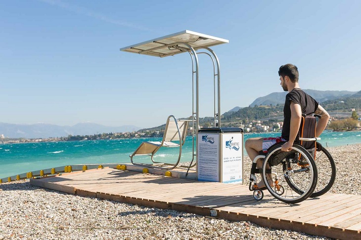 Erişilebilir plajda, denize tekerlekli sandalyesi ile ilerleyen bir engelli birey objektife yansıyor.