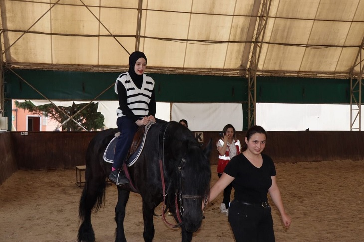 Rehberin kontrolünde, ata binme heyecanı yaşayan bir kız çocuğu objektife yansıyor.