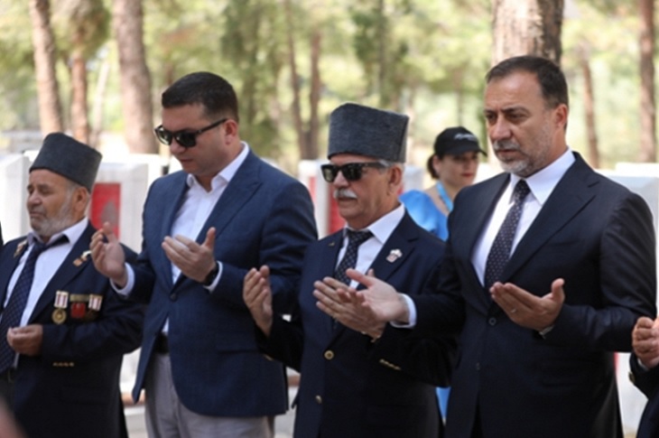 Şehitlerin kabrinde aynı anda dua eden katılımcılar objektife yansıyor.