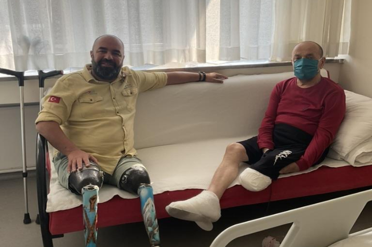 Dalış rekortmeni Ufuk Koçak, hastane odasında sol bacağı ampute edilen erkek depremzede ile koltukta oturuyor.