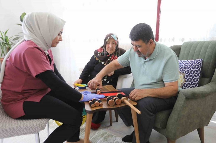 Sağlık görevlisinin kontrolüyle evde fizik tedavisi olan bir yaşlı adam objektife yansıyor.