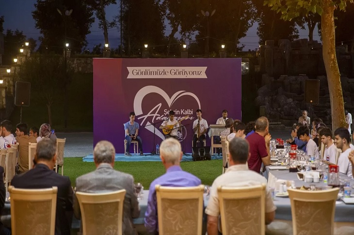 Yemek masalarındaki çok sayıda katılımcı ve sahnede konser veren 4 görme engelli genç birey objektife yansıyor.