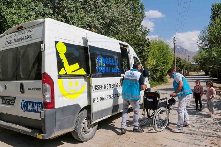 İki görevlinin özel hizmet aracından tekerlekli sandalyeyi indirdiği ana dair bir görüntü objektife yansıyor.