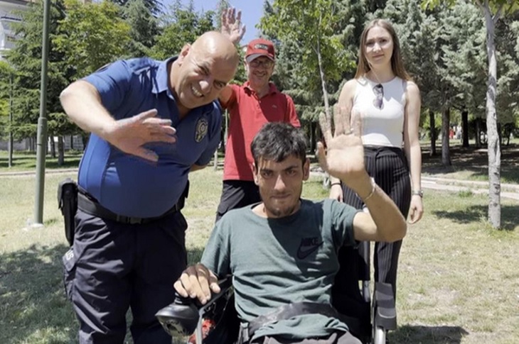 Akülü sandalyesine binen genç, polis memuru Mustafa Şahin ile birlikte objektife el sallıyor.