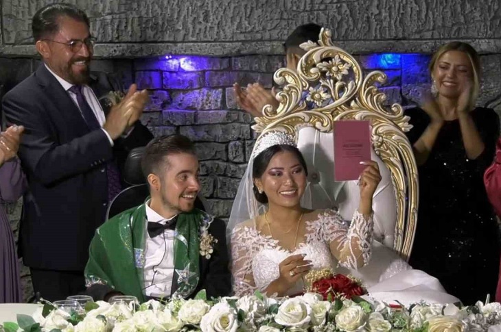 Nikah işlemi sonrası aile cüzdanını eline alan gelinin ve damadın sevinci objektife yansıyor.