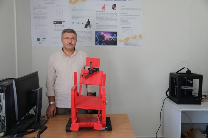 Doç. Dr. Mehmet Barış Tabakcıoğlu, çalışmaları devam eden maket tekerlekli sandalye ile birlikte objektife yansıyor.