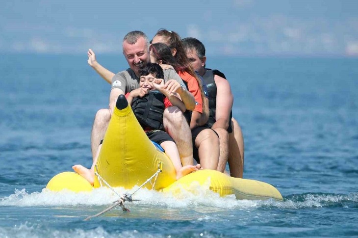 Özel gereksinimli bireylerle birlikte denizdeki şişme muza binen Başkan Tahir Büyükakın objektife yansıyor.