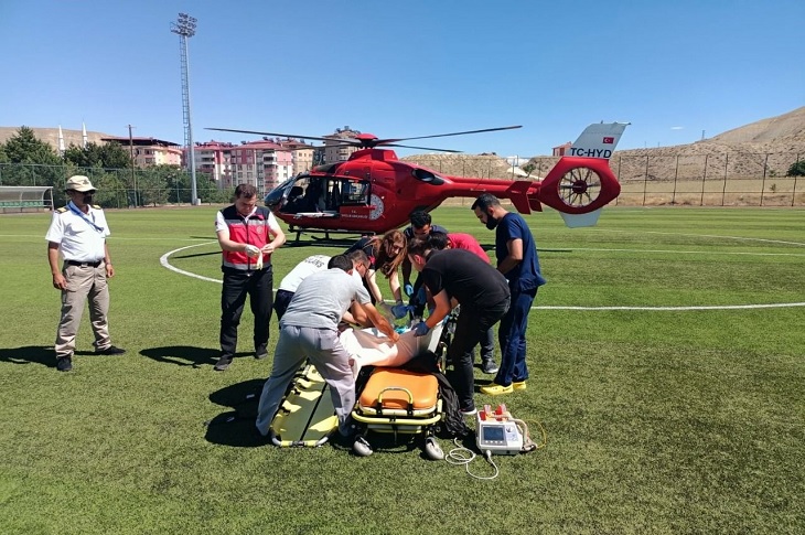 Sedye üzerindeki astım hastası kadını şehir stadına inen ambulans helikoptere transfer eden sağlık görevlileri objektife yansıyor.