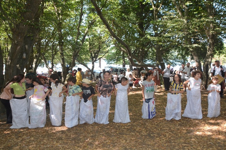 Ormanlık bölgede, çuval yarışı için yan yana dizilen çok sayıda çocuk objektife yansıyor.