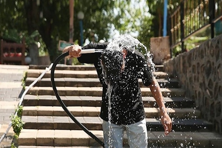 Bunaltıcı havada başını hortumdan akan suyla yıkayan bir birey objektife yansıyor.