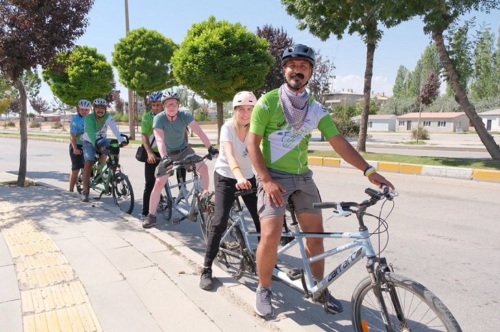 Yol üzerinde mola veren bir grup bisiklet sürücüsü objektife yansıyor.