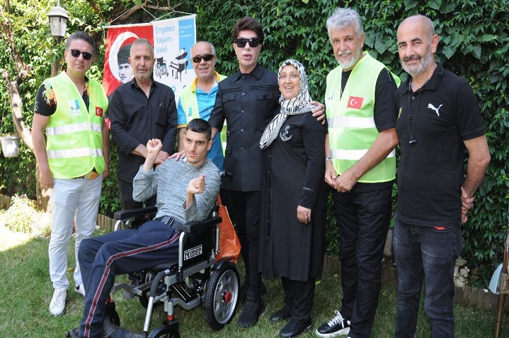 Akülü sandalye teslimi sonrası aile ile çekilen bir toplu hatıra resmi objektife yansıyor.