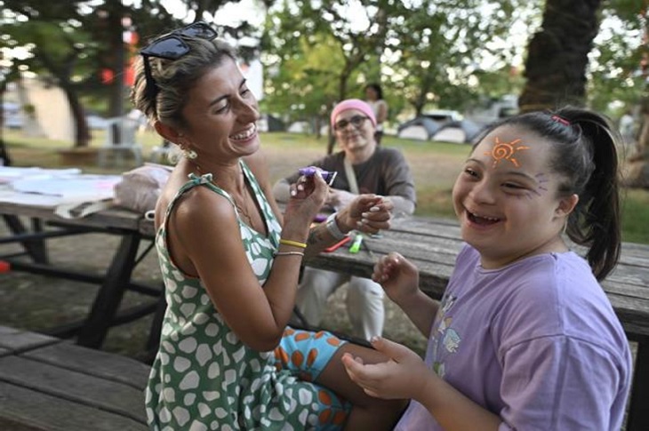 Yüzüne renkli kalemlerle şekiller çizilen bir Down Sendromlu kızın sevinci objektife yansıyor.