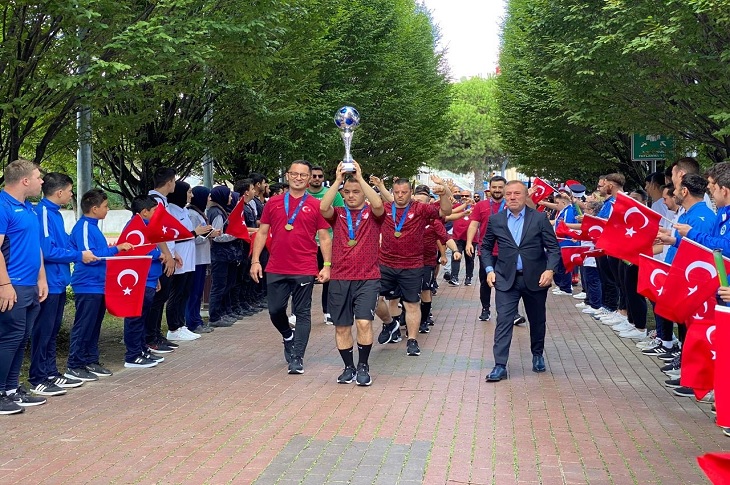 Türk bayrağı sallayan vatandaşların oluşturduğu koridorda, ellerindeki kupayla ilerleyen milli takım kadrosu objektife yansıyor.