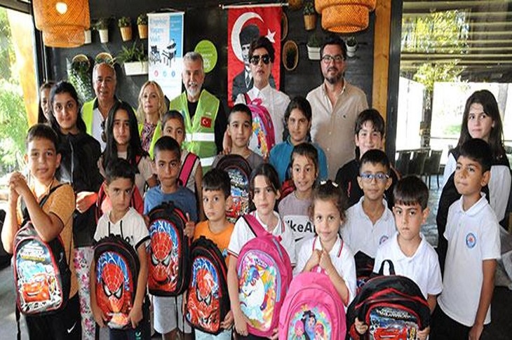 Yılmaz Morgül'ün çanta ve okul malzemelerini teslim alan çok sayıda öğrenci ile birlikte çekilen bir toplu hatıra resmi objektife yansıyor.