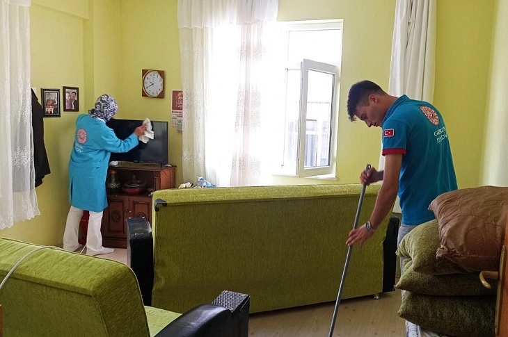 İhtiyaç sahibinin salonunu temizleyen 2 görevli objektife yansıyor.