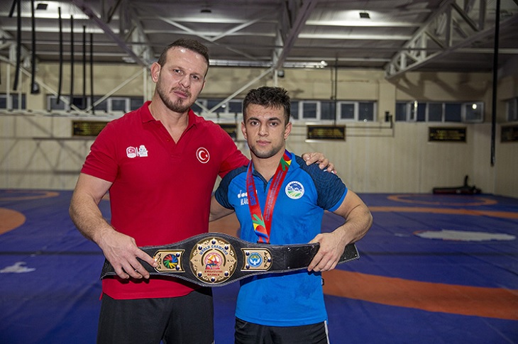 Başarılı sporcu, kazandığı kemer, madalya ve yanındaki hocasıyla birlikte objektife yansıyor.