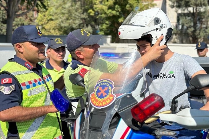 Park halindeki motorsiklete binen bir engelli çocuğa koruyucu kaskı takan jandarma görevlileri objektife yansıyor.