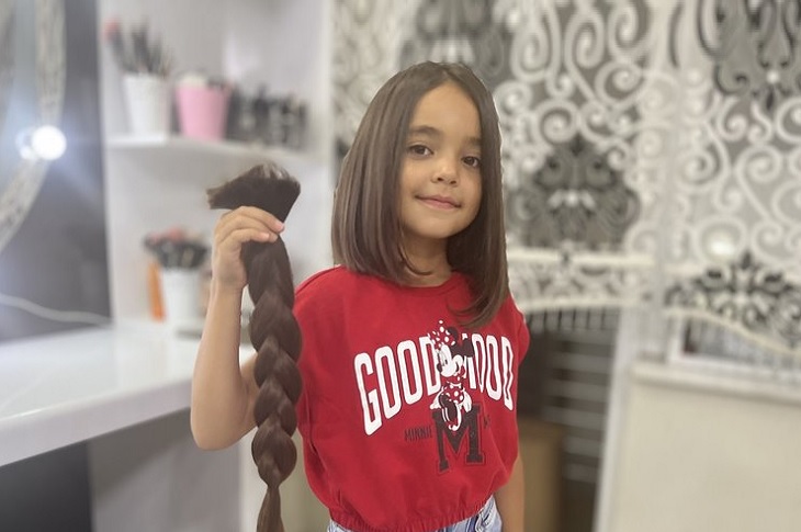 8 yaşındaki Azra, elinde kestirdiği örgülü saçıyla birlikte objektife yansıyor.