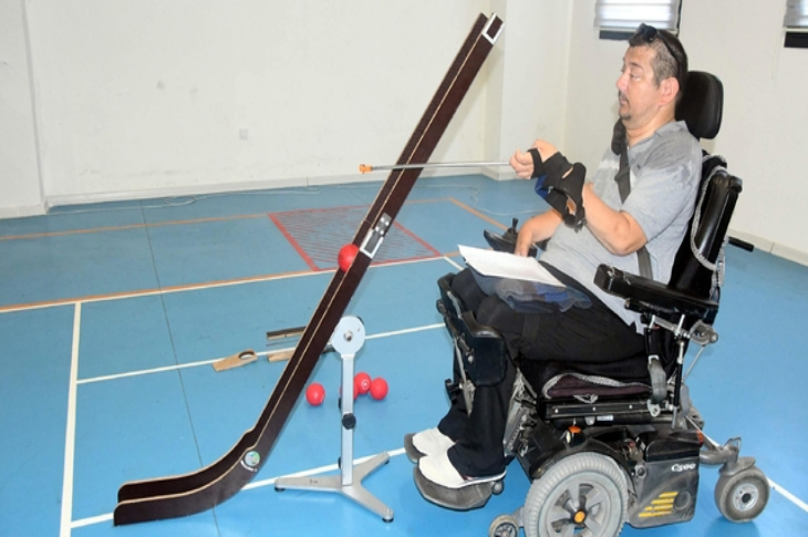 Bocce sporcusu Bilgin Can tekerlekli sandalye de oturarak, önünde bulunan bocce şut aparatı ile antrenman yapıyor.